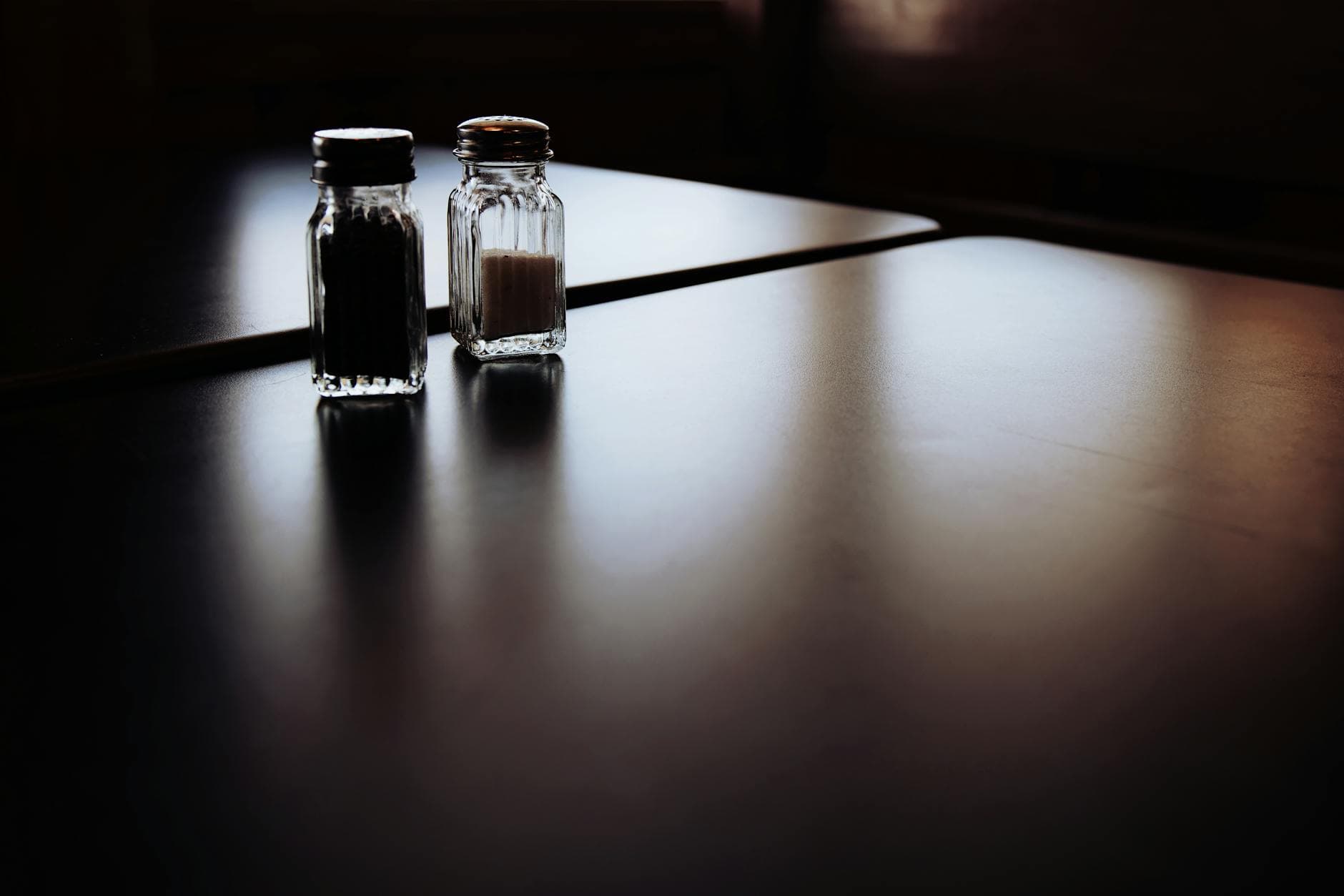 A moody still life of salt and pepper shakers on a dimly lit table.