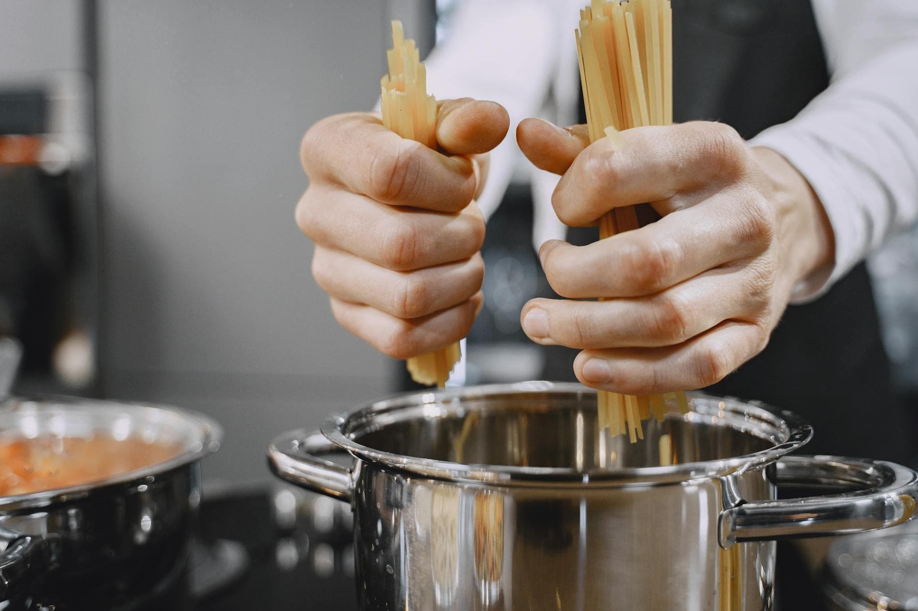 Close-up of chef's hands adding pasta to a boiling pot in a kitchen.