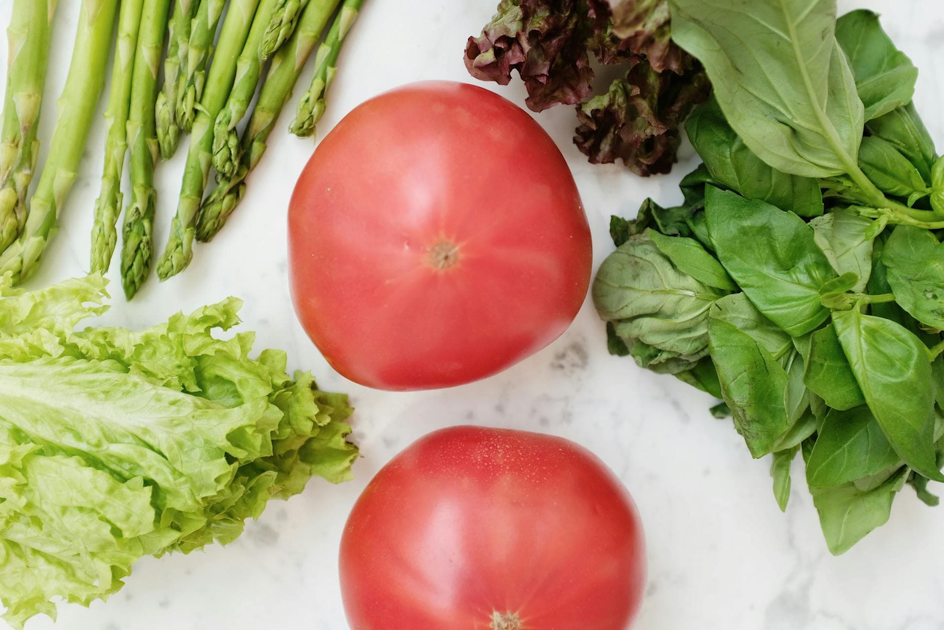 A vibrant collection of fresh vegetables including tomatoes, asparagus, and leafy greens on a marble surface.