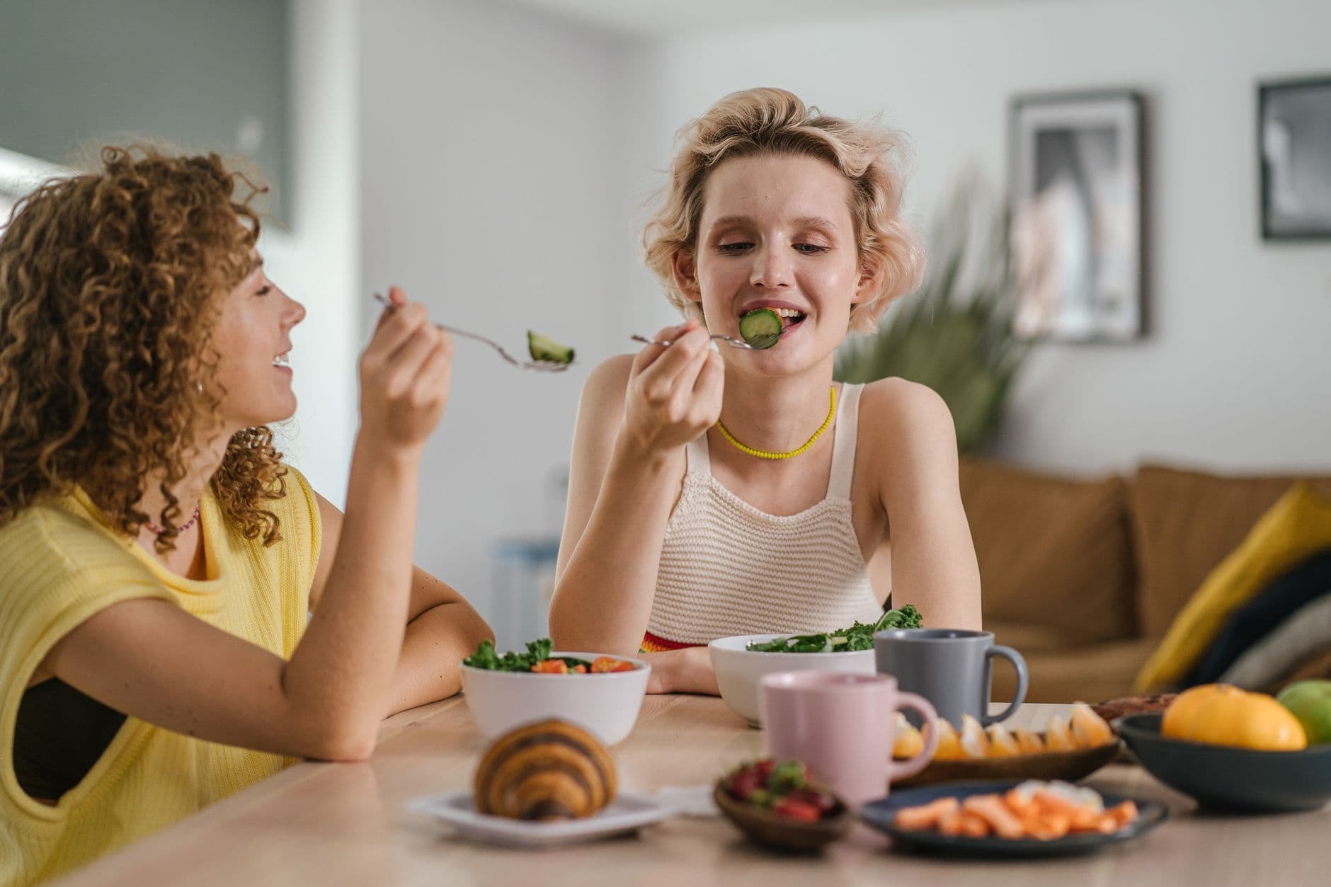 Two women enjoying a healthy meal at a cozy dining table, sharing a joyful indoor breakfast moment.