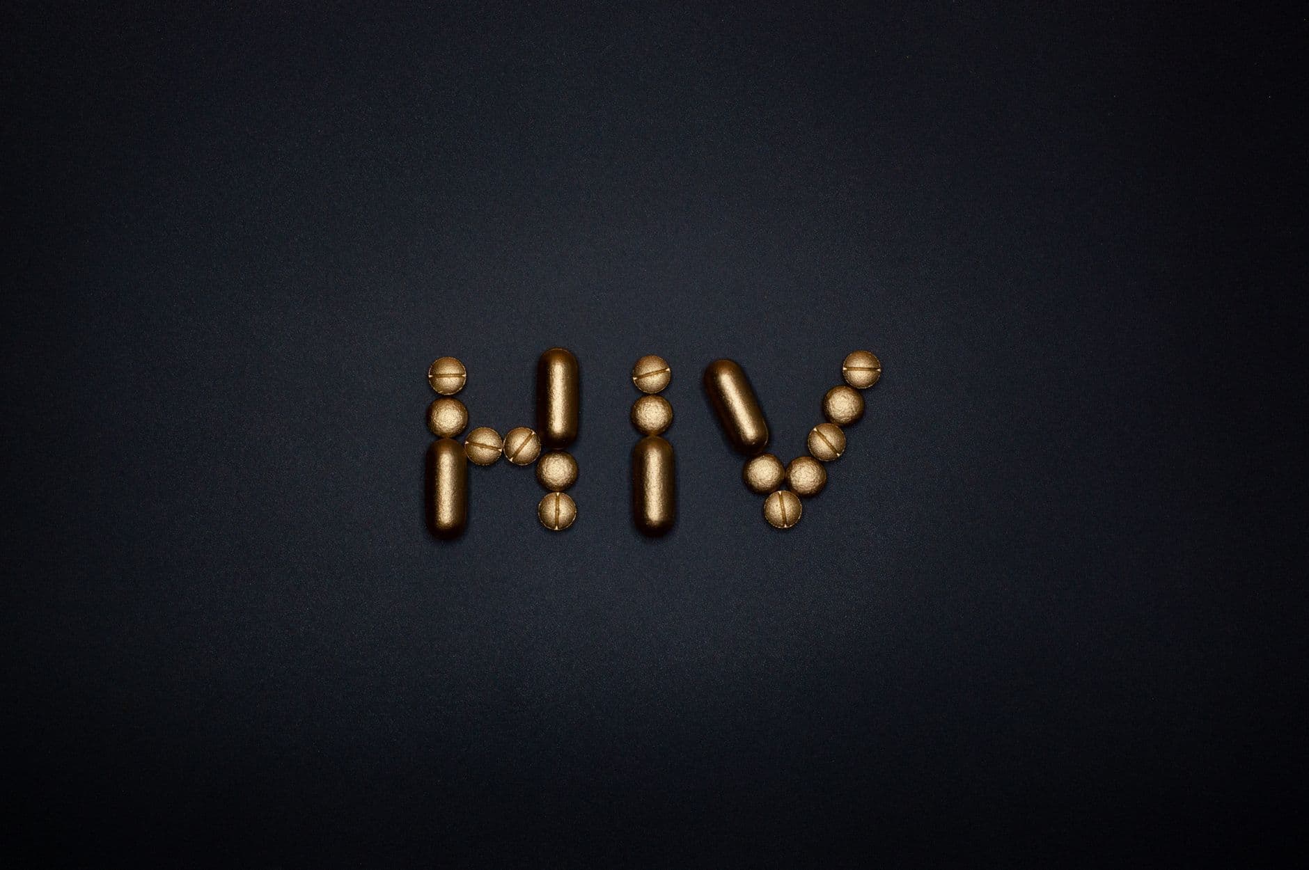 Golden capsules form the word HIV on a dark background, symbolizing healthcare and treatment.