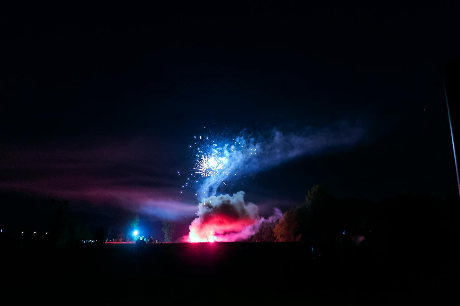 A colorful fireworks display lighting up the dark night sky over a landscape with smoke and silhouettes.