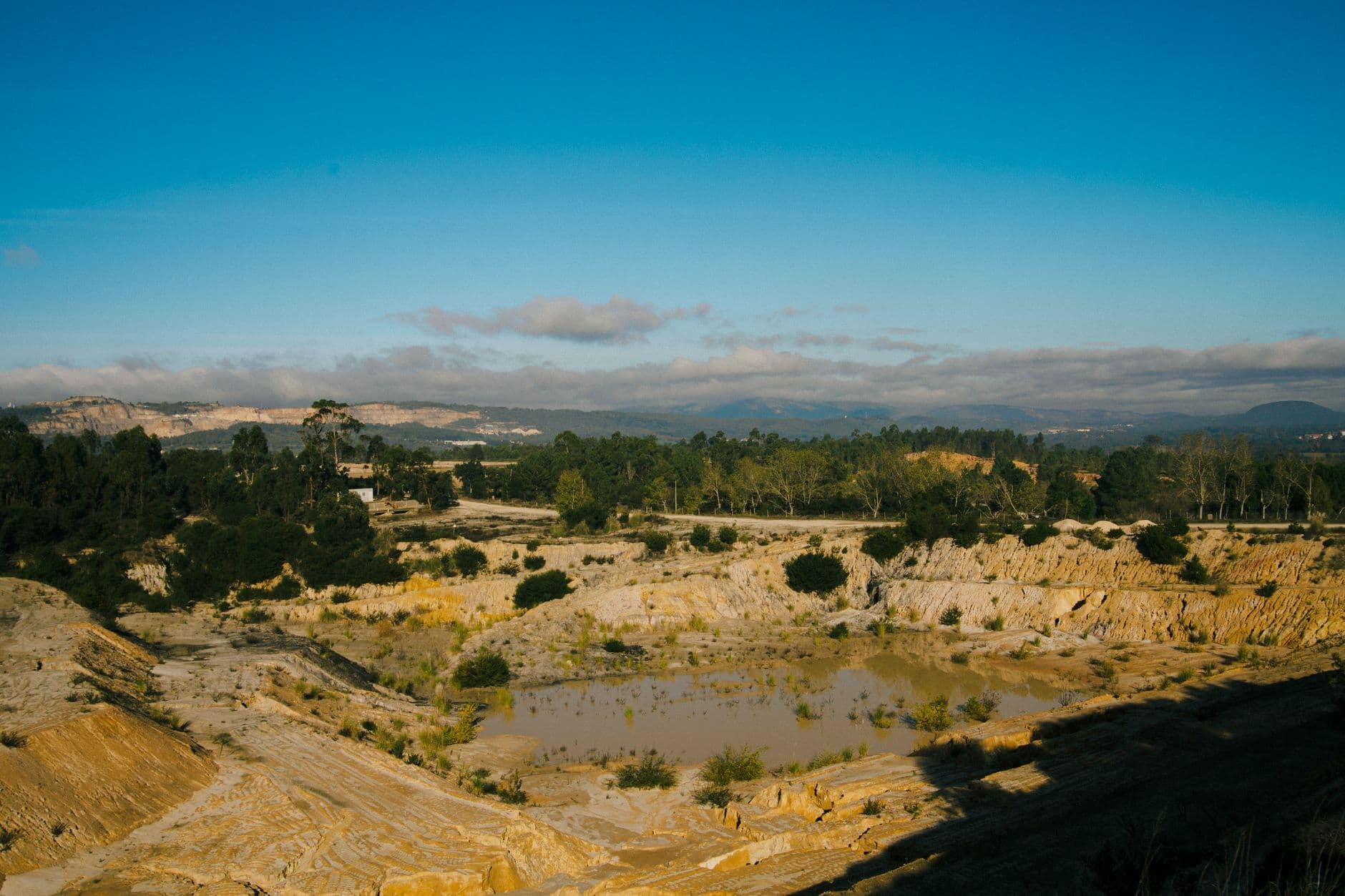 Serene quarry landscape with clear blue skies, surrounded by lush forest and rocky terrain.